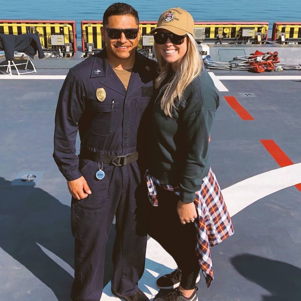Katie Piedra of Operation Gratitude standing on a Navy ship with her husband who is wearing his Navy uniform