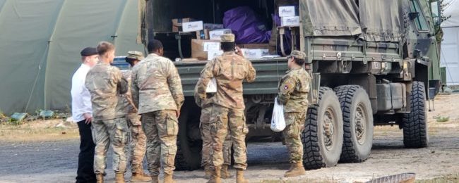 Service members standing by a military vehicle unloading Operation Gratitude boxes.