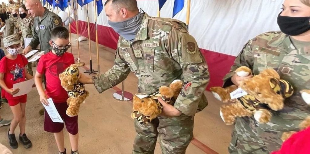 Service members hand out teddy bears to military children.