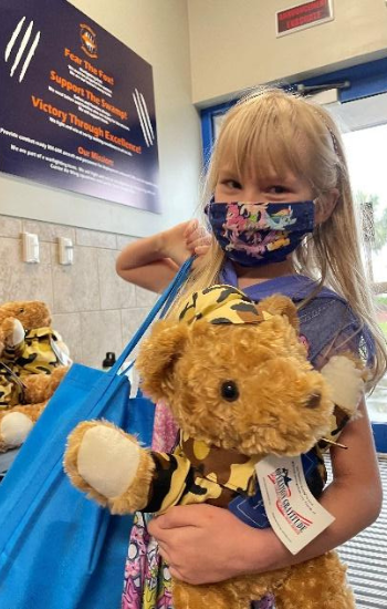 Young girl standing with an Operation Gratitude Battalion Buddy bear.