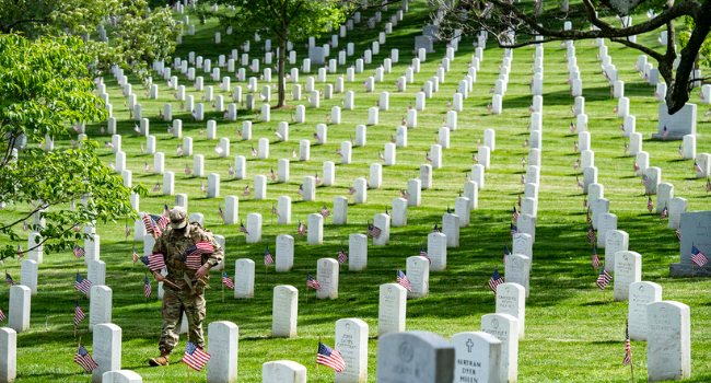 US Army soldier placing flags on gravestones at Arlington Cemetery for Memorial Day 2021.