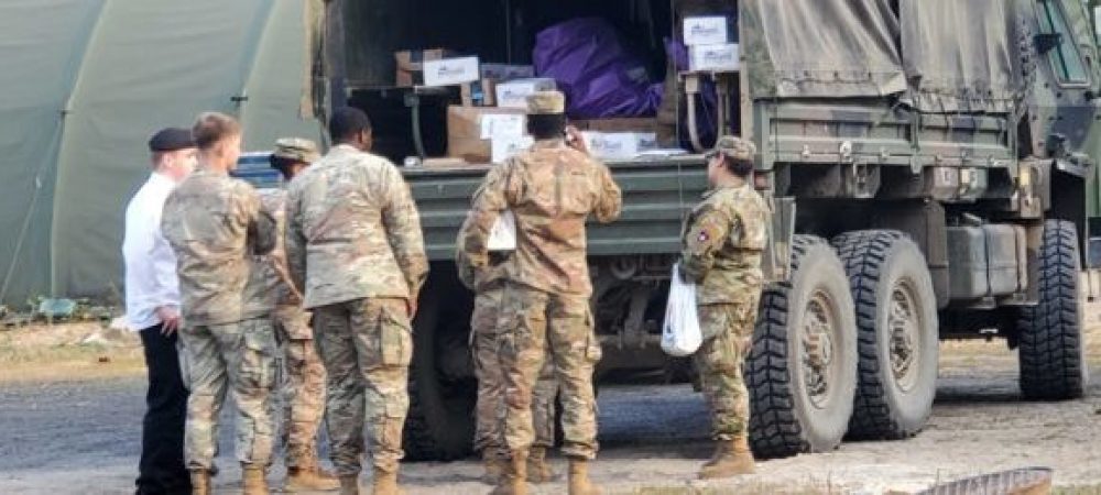 Service members standing by a military vehicle unloading Operation Gratitude boxes.